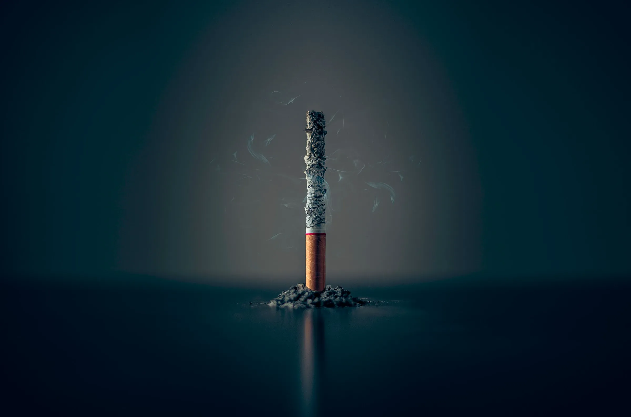 Une cigarette consumée jusqu’au filtre, debout sur un petit tas de cendres, sur un fond bleu nuit.