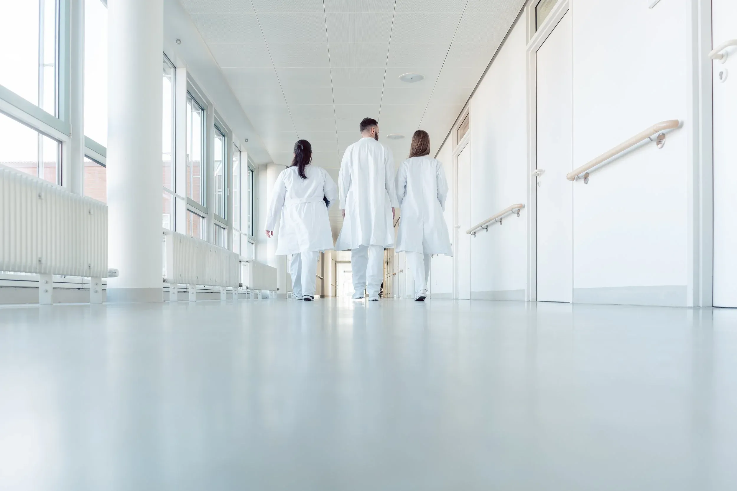 Trois soignant·e·s en blouse blanche, de dos, dans un couloir d’hôpital
