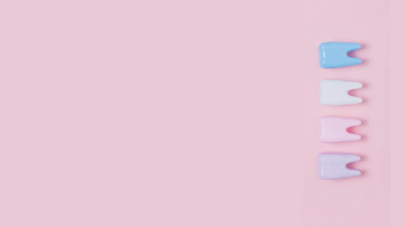Quatre dents miniatures, bleue, blanche, rose et mauve, alignées sur un fond rose