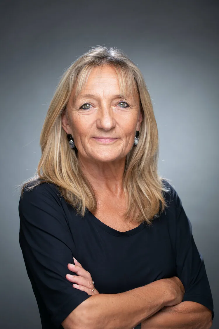 Portrait photographique de Marta Hegyaljai Python, formatrice en hypnose à Fribourg, bras croisés, regardant l’objectif sur un fond gris.