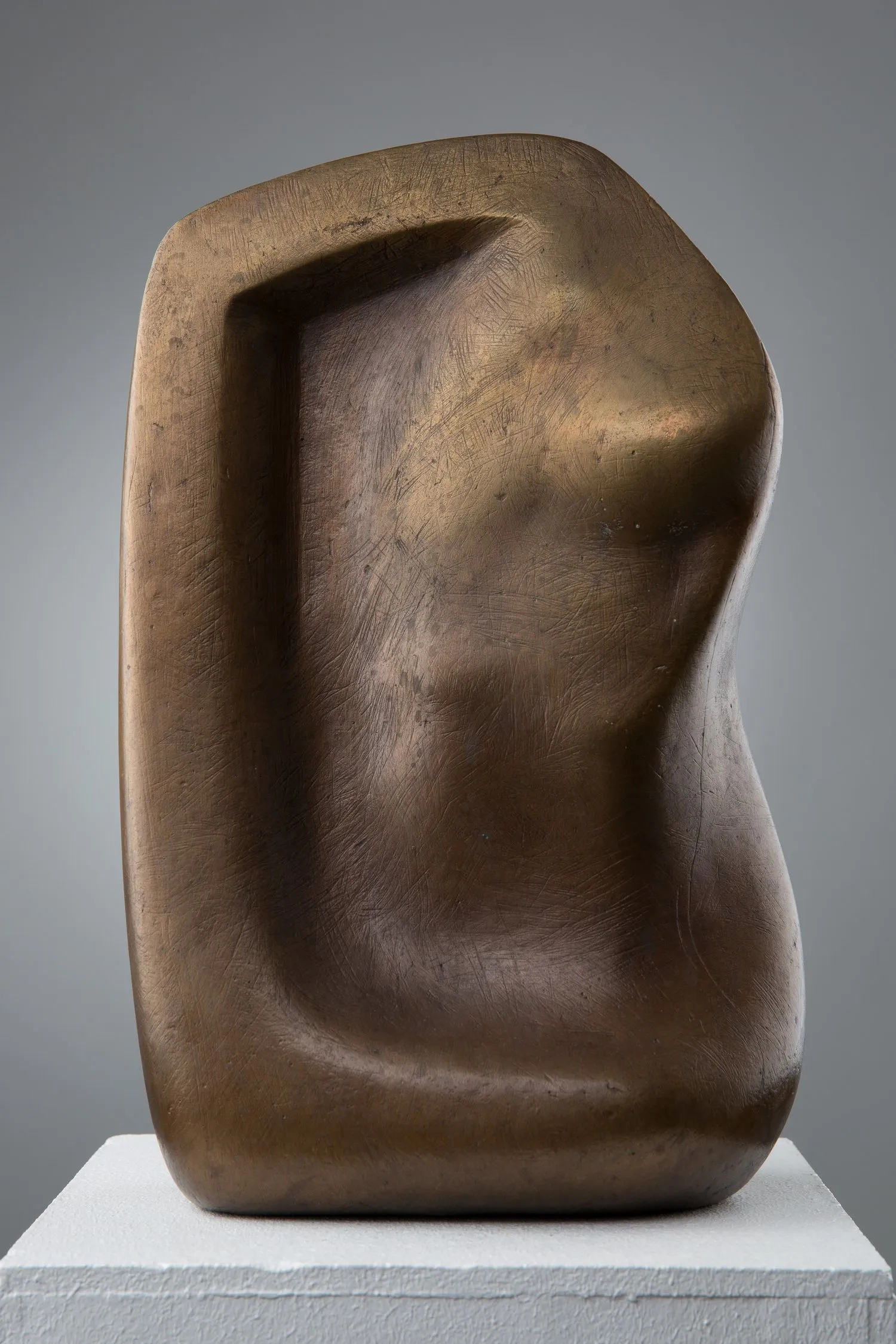 « Metamorphose IV » de Jan Hegy : sculpture abstraite en métal patiné, forme organique arrondie creusée d’un profond renfoncement vertical, posée sur un socle blanc.